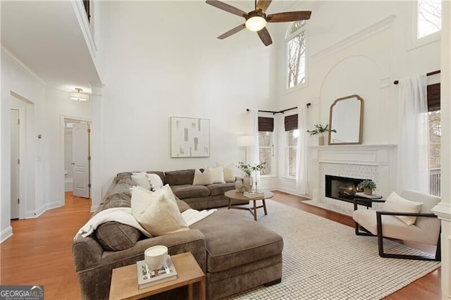 living room with a ceiling fan, a high ceiling, a fireplace with flush hearth, and wood finished floors