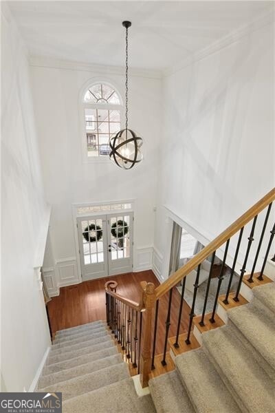 stairway featuring wood finished floors, french doors, crown molding, a decorative wall, and a notable chandelier