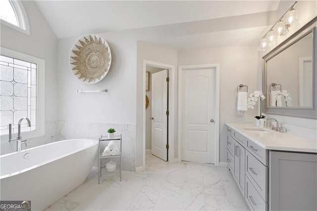 bathroom with a wealth of natural light, a freestanding bath, marble finish floor, and vanity