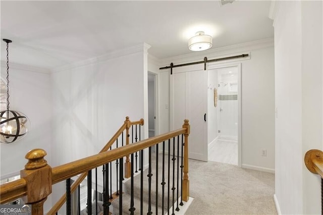 hall with a barn door, an upstairs landing, ornamental molding, and carpet flooring