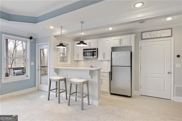 kitchen featuring stainless steel microwave, freestanding refrigerator, a breakfast bar area, white cabinets, and decorative backsplash