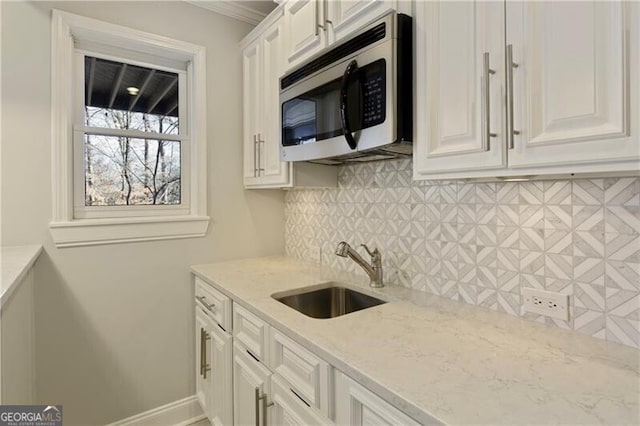 kitchen featuring a sink, stainless steel microwave, tasteful backsplash, white cabinets, and light stone countertops