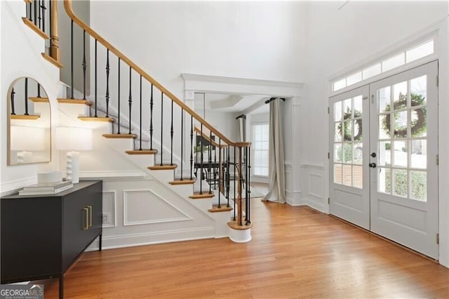 entryway with stairway, wood finished floors, a decorative wall, and french doors