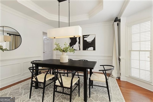 dining room with a wainscoted wall, ornamental molding, wood finished floors, a decorative wall, and a raised ceiling