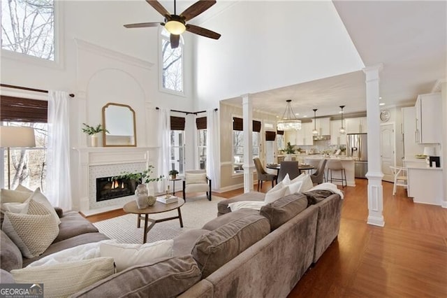 living area with a wealth of natural light, decorative columns, a glass covered fireplace, and light wood-style flooring