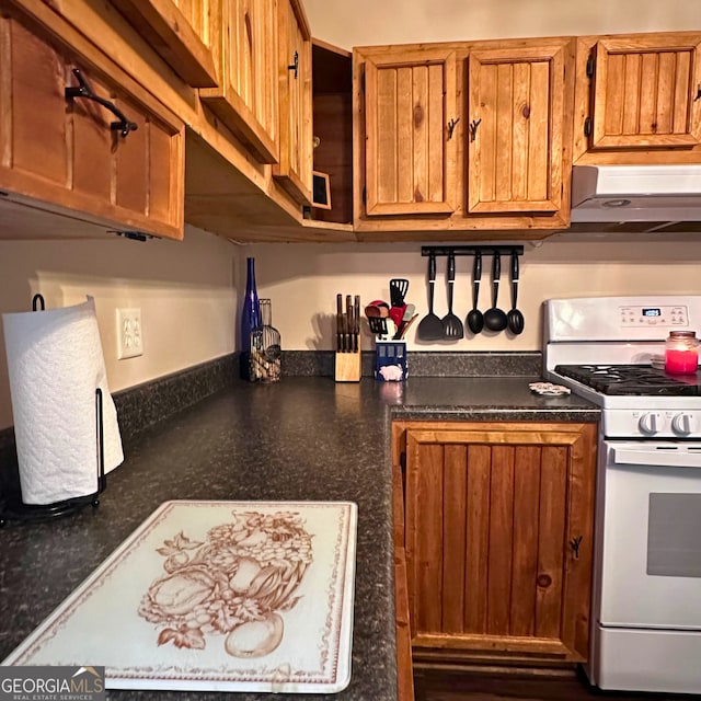 kitchen featuring under cabinet range hood, brown cabinets, dark countertops, and gas range gas stove