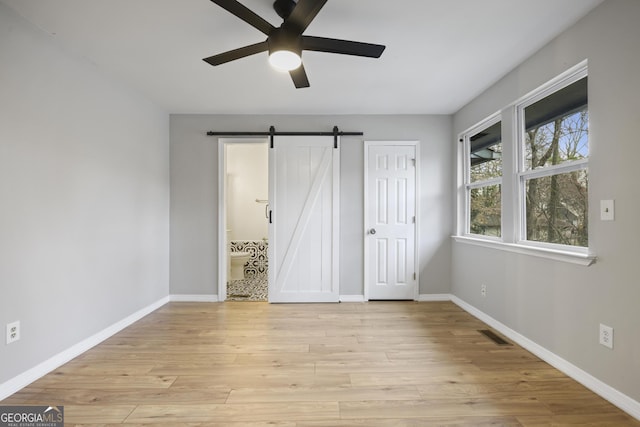 unfurnished bedroom with visible vents, ensuite bath, a barn door, light wood-style floors, and baseboards