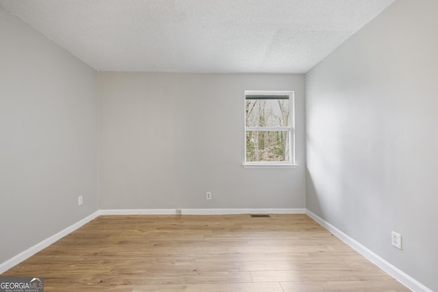 spare room with baseboards, light wood-style floors, and a textured ceiling