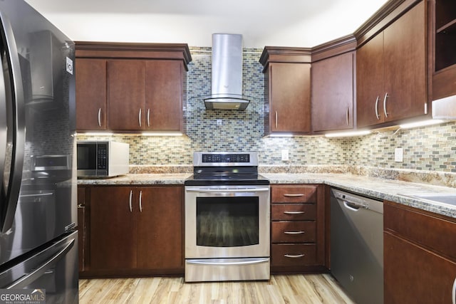 kitchen with light stone counters, wall chimney range hood, backsplash, stainless steel appliances, and light wood finished floors