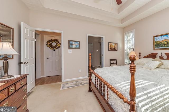 bedroom featuring light carpet, ensuite bathroom, a raised ceiling, and baseboards