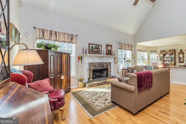 living area with baseboards, high vaulted ceiling, a fireplace, ceiling fan, and wood-type flooring