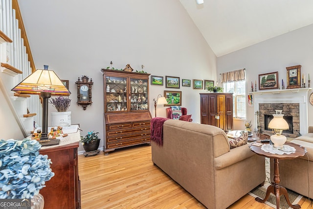 living area with a stone fireplace, stairway, light wood-type flooring, and high vaulted ceiling