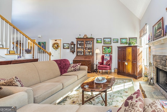 living room with stairs, high vaulted ceiling, a fireplace, and light wood finished floors