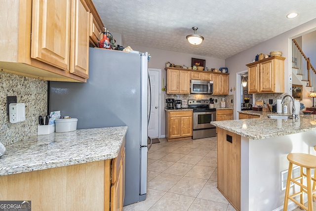 kitchen featuring a sink, stainless steel appliances, a peninsula, a breakfast bar area, and light tile patterned floors