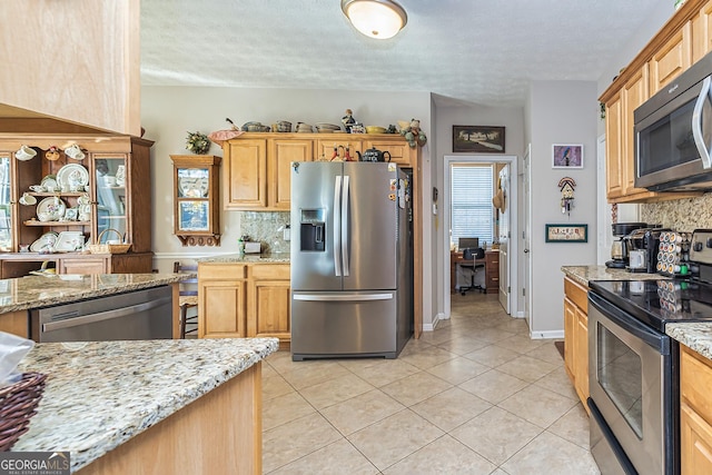 kitchen featuring light tile patterned floors, light stone countertops, tasteful backsplash, and appliances with stainless steel finishes