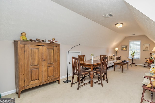 dining room featuring visible vents, baseboards, lofted ceiling, light carpet, and a textured ceiling