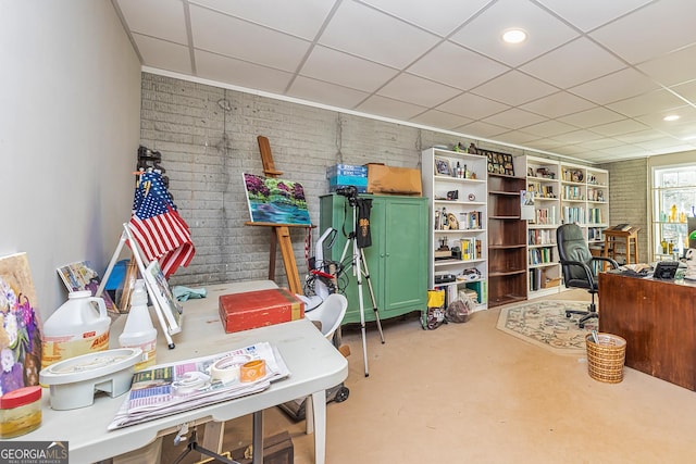 office with a drop ceiling, concrete floors, and brick wall