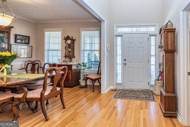 foyer with light wood finished floors, baseboards, and ornamental molding