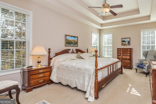 bedroom featuring a tray ceiling, multiple windows, light colored carpet, and a ceiling fan