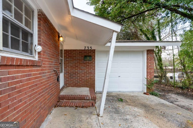 entrance to property with brick siding, concrete driveway, a garage, and fence