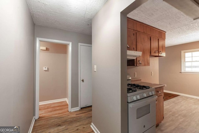 kitchen with baseboards, under cabinet range hood, light wood-type flooring, white range with gas cooktop, and a textured ceiling