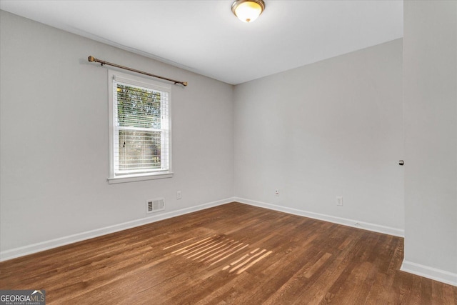 spare room featuring wood finished floors, visible vents, and baseboards