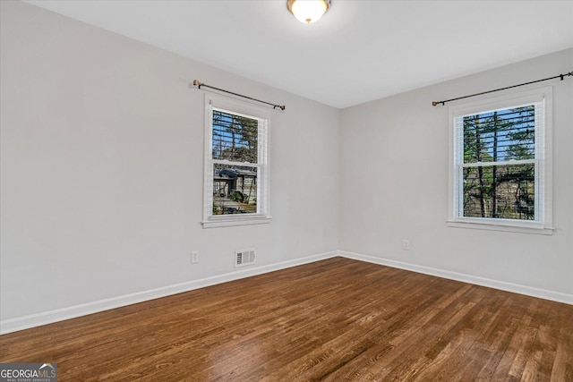 spare room featuring visible vents, plenty of natural light, baseboards, and dark wood finished floors