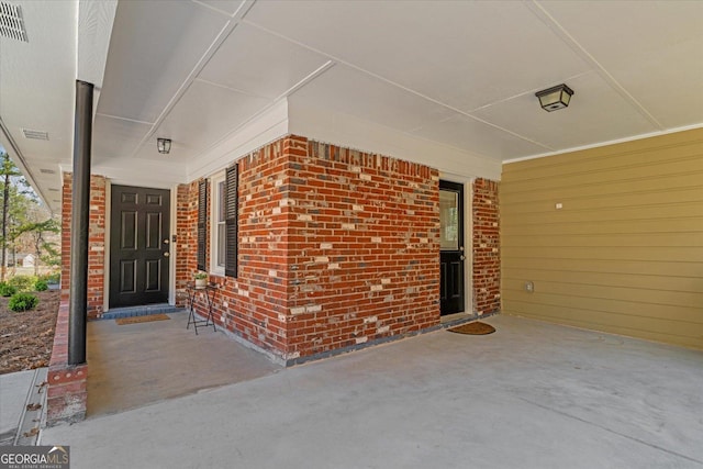 property entrance featuring visible vents, brick siding, and covered porch