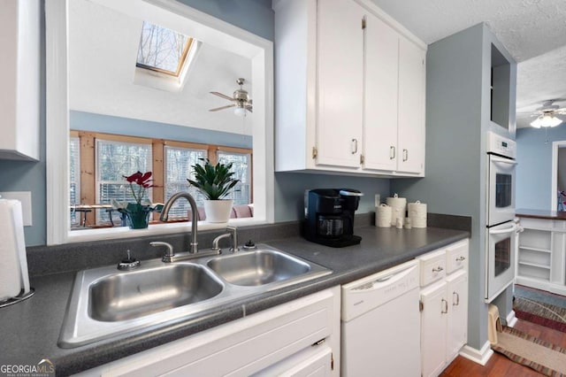 kitchen featuring white appliances, ceiling fan, a sink, white cabinetry, and dark countertops