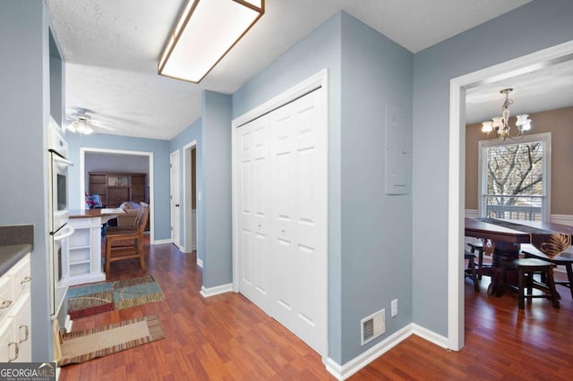 hall featuring visible vents, electric panel, wood finished floors, baseboards, and a chandelier