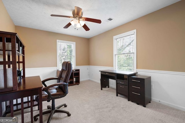 office space featuring visible vents, baseboards, light carpet, a textured ceiling, and a ceiling fan