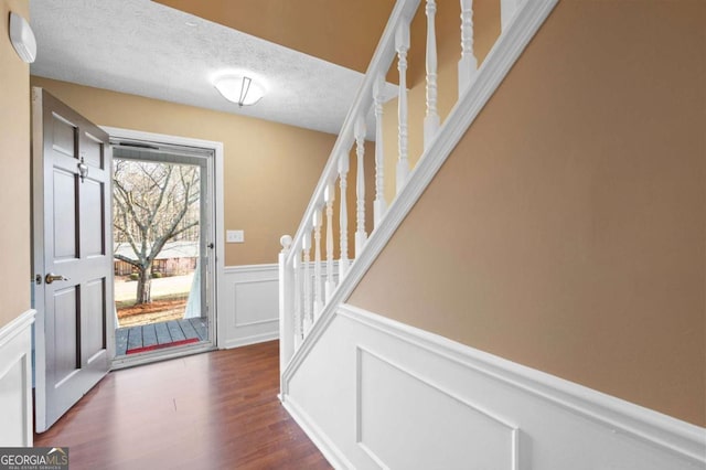 foyer with a textured ceiling, stairway, wood finished floors, wainscoting, and a decorative wall