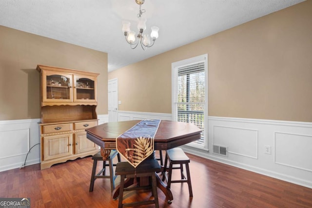 dining area featuring visible vents, a notable chandelier, a wainscoted wall, and dark wood-style flooring