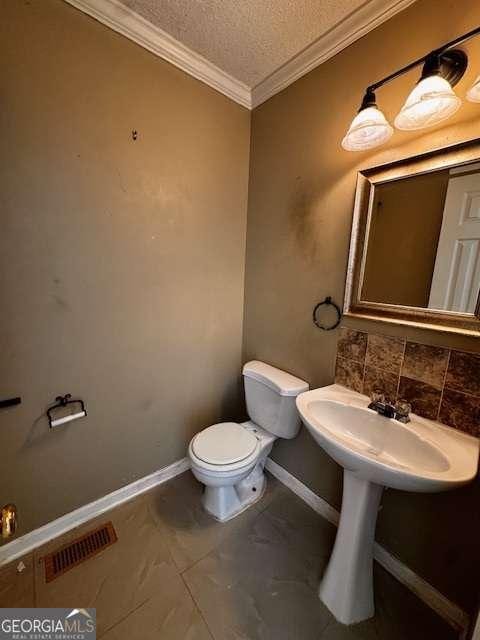 half bath featuring visible vents, toilet, ornamental molding, a textured ceiling, and baseboards