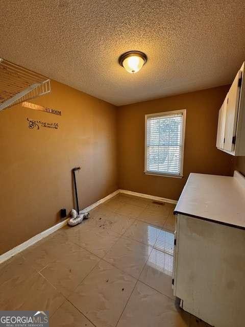 laundry room with cabinet space, a textured ceiling, and baseboards
