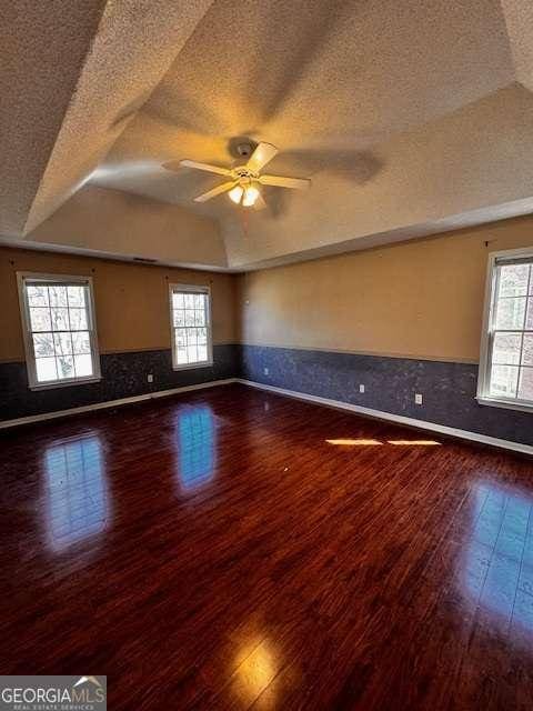 unfurnished room with a wainscoted wall, plenty of natural light, a raised ceiling, and wood-type flooring