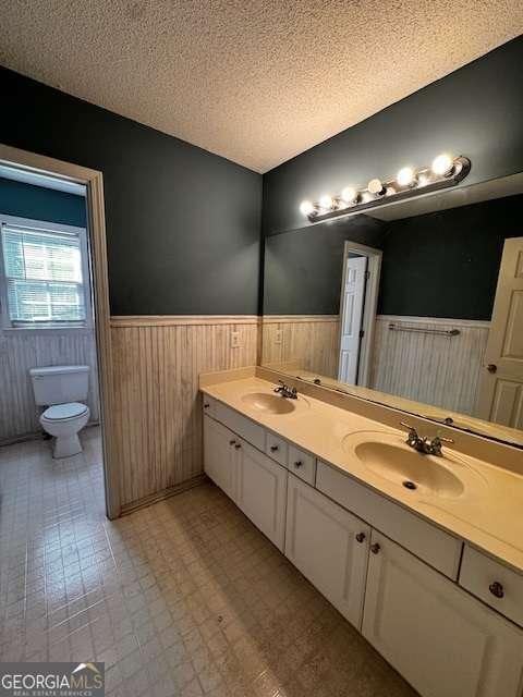 bathroom featuring wainscoting, a textured ceiling, toilet, and a sink