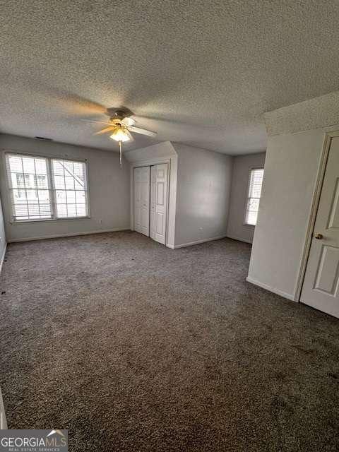 unfurnished bedroom featuring baseboards, carpet floors, ceiling fan, a closet, and a textured ceiling