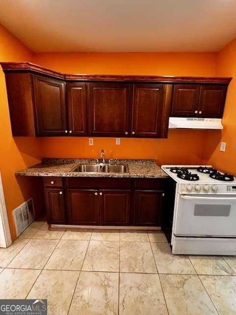 kitchen featuring visible vents, under cabinet range hood, a sink, gas range gas stove, and dark brown cabinets