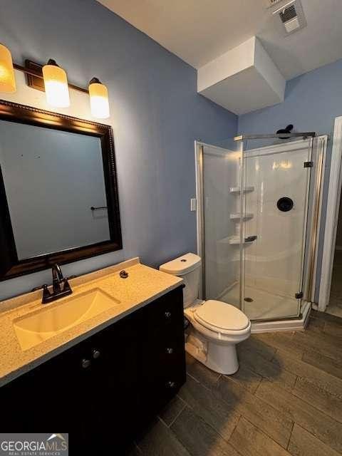 bathroom with visible vents, a shower stall, toilet, wood finished floors, and vanity