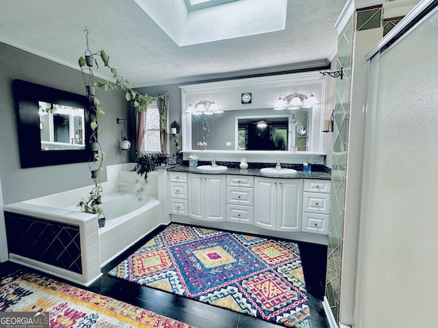 full bath with double vanity, a textured ceiling, a bath, a skylight, and a sink