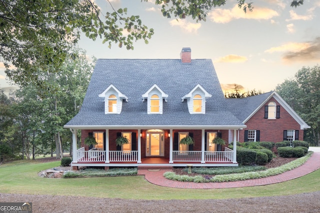 new england style home featuring brick siding, a porch, a front lawn, and a shingled roof