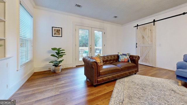 living room featuring visible vents, crown molding, baseboards, a barn door, and wood finished floors