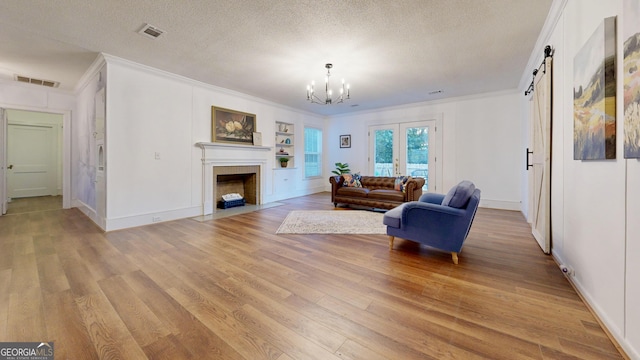 living area with visible vents, a fireplace with flush hearth, a barn door, light wood-style flooring, and a textured ceiling