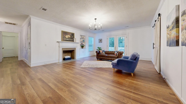 living room with visible vents, ornamental molding, light wood-type flooring, a chandelier, and a textured ceiling