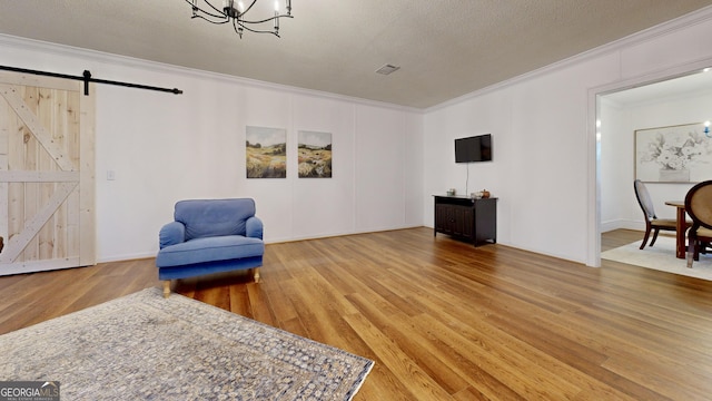 sitting room with a barn door, a notable chandelier, crown molding, and wood finished floors