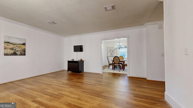 unfurnished room with light wood-style floors, visible vents, an inviting chandelier, and ornamental molding