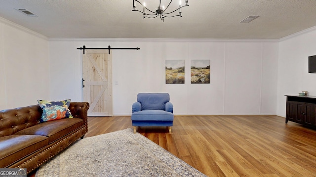 living area featuring visible vents, an inviting chandelier, a barn door, crown molding, and wood finished floors