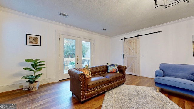 living room with visible vents, ornamental molding, a barn door, and wood finished floors