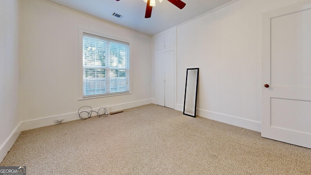carpeted spare room with ornamental molding, visible vents, and a ceiling fan